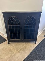Front view of the black MDF cabinet with decorative metal grill doors.