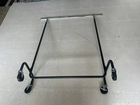 Top-down view of black metal rolling clothing rack with square base and caster wheels on light surface.