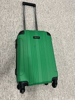 Closed view of green hard shell luggage with telescoping handle extended, showing dresser-textured exterior and corner protectors