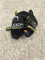 Pair of CCM youth large elbow pads, black with yellow accents, placed on carpet.