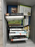 Top-down view of a box filled with paperback books showing various titles and authors arranged horizontally and vertically.