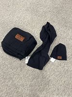 Full set of dark blue knit throw blanket, scarf, and beanie displayed on carpet.