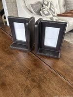 Pair of dark brown synthetic leather bookend picture frames standing on a wooden surface with visible white stitching and 4x6 inch photo openings.