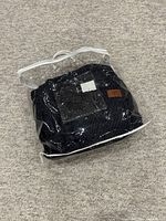 Throw blanket folded inside clear plastic packaging with visible knit texture and brown leather patch.