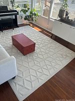 Full view of ivory geometric patterned rug in a room setting with wooden floor, a piano, and furniture.