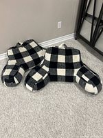 Two large black and white checkered fleece floor pillows designed with arm rests and back support, placed on carpeted floor.