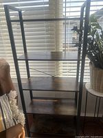 Full front view of the bookshelf showing five evenly spaced dark wood shelves within a black metal frame structure by a window.