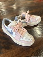 Photo showing side and top view of white and pink Nike Air sneakers on wooden surface.