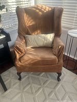 Front view of camel microfiber armchair with wingback design, showing cushion and wooden cabriole legs, placed near window with natural light.