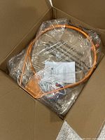 Photo of the orange steel basketball hoop rim with attached mounting bracket and hardware in a plastic bag inside a cardboard box.