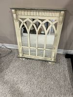 Front view of vintage farmhouse wall mirror leaning against a wall, showing distressed paint, wood frame details, and hooks.