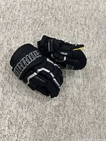 Pair of black and yellow Warrior Covert QRS1 hockey gloves lying on a carpeted floor showing the top side with 'Warrior' and 'Covert' branding.