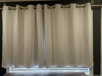 Full view of two white curtain panels hung with metal grommets over a window.