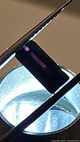 Close-up image of a rectangular, octagon-cut deep dark purple tourmaline held with tweezers over a light source, showing color and clarity details.
