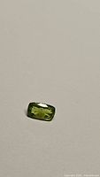 Natural cushion cut green peridot gemstone shown on a neutral background for color and clarity assessment.