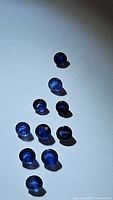Image showing eleven natural round cut blue sapphires arranged on a white surface, various sizes, appearing deep saturated blue color with some reflections.