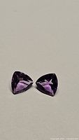 Pair of natural purple amethyst trillion cut gemstones with deep color and high clarity laid flat on neutral background.
