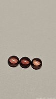 Three small round cabochon gemstones with deep orange purple coloration, arranged in a row on a grey background