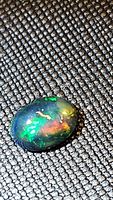 Close-up front angle of 1.22 carat oval cabochon cut natural Ethiopian black opal showing bright multicolored flashes.