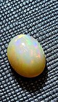 Oval cabochon Ethiopian opal gemstone with visible multicolored play-of-color flash on textured background.