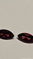 Pair of natural marquis cut garnet gemstones showing red-orange color and clarity from a flat angle.