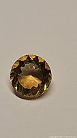 Close-up photo of the round step-cut natural golden citrine gemstone showing its facets and color.