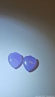 Two natural lavender jade heart-shaped gemstones on a neutral background, showing their shape and color.