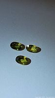 Three natural oval cut sapphires with a golden yellow-green color laid out on a white background.