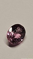 Close-up photo of natural oval cut pink spinel gemstone showing facets and pink hues under lighting.