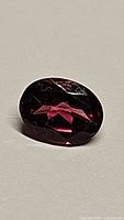 Close-up photo of an oval cut purple-pink rhodolite garnet gemstone showing facets and clarity.