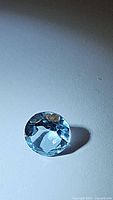 Photo of a round faceted natural sky blue topaz gem, showing bright sky blue color and light reflection.