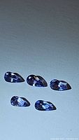 Five pear-shaped natural tanzanite gemstones laid out on a flat surface, showing size and facets.