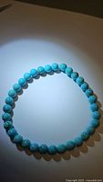 Top view of the turquoise bead bracelet arranged in a circle on a white background under bright light, showing the smooth surface and natural stone matrix details on some beads.