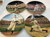 Four porcelain baseball plates featuring vintage baseball players in various action poses on a baseball field. Plates have crowd backgrounds and gold rims.