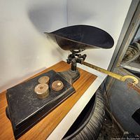 Full view of the heavy cast iron scale with its large concave weighing pan and brass indicator arm, showing the scale and included weights on the base.