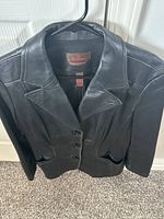 Another angle of black leather jacket on hanger highlighting shoulders and collar seam.
