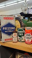 Group photo of four vintage automotive tins on shelf: large Prestone Anti-Freeze can, green Quaker State Motor Oil can, red and beige Wynn's Gasoline Treatment can, and small Canadian Tire oil can in front.