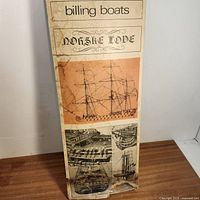 Front view of the box with brand and model name 'Billing Boats Norse Lore' and vintage sketches of the ship model and details.