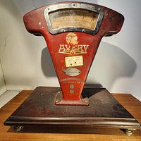 Front view of vintage Avery scale showing red metal body, large dial with glass cover, Avery logo and metal platform base.