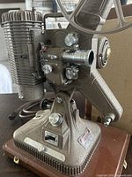 Close-up view of vintage Keystone Regal K 109 8mm movie projector showing metal textured finish, adjustment knobs, lens, and reel arm.