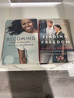 Two hardcover books side by side: 'Becoming' by Michelle Obama and 'Finding Freedom' about Harry and Meghan.