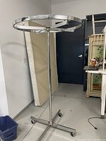 Full view of a round metal clothing rack with circular top and vertical central support on caster wheels.