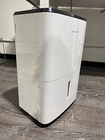 Side and front view showing white body, water bucket with translucent window, and black top panel with digital display and vents.