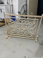 Photo showing front view of the vintage iron fireplace grill with ornamental scrollwork and cream finish.