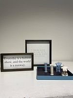Two framed quote signs and a blue tray with four ceramic figurines on a white surface against a neutral background.