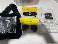 Overview of the sunglasses with yellow Shady Lady cases, the black faux fur bag, and small jewelry organizer with accessories including hair pin and anklet.