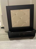 Front view of wall-mounted mail holder showing black frame, white padded back board with metal buttons, and lower tray for holding mail.