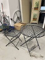 Full view of black metal bistro chair and round table with lattice pattern, placed indoors on a concrete floor.