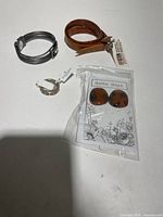 Top-down view of all four jewelry pieces showing the ring, pair of earrings, brown leather bracelet, and black braided bracelet on a white surface.