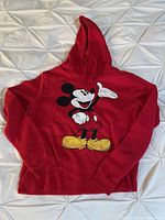 Red hooded sweatshirt with large Mickey Mouse graphic on front, laid flat on white background.
